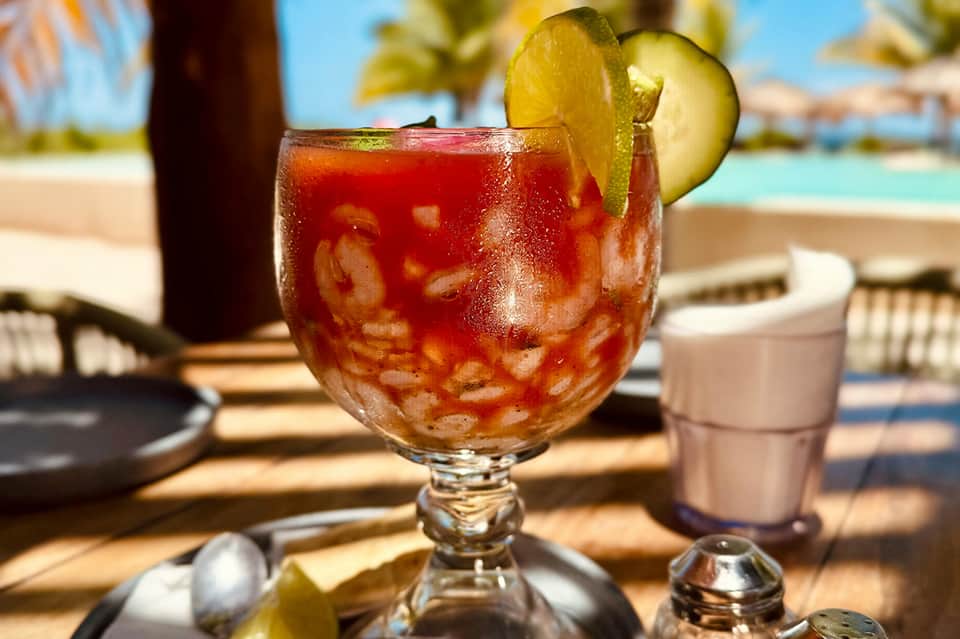 Tropical cocktail with lime garnish on beach table overlooking turquoise ocean and palm trees