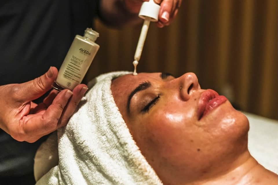 Spa treatment with therapist applying serum to client's face with brush, client wearing white head wrap