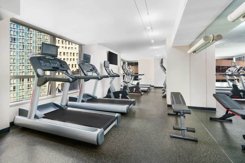 Modern fitness center with treadmills, exercise bikes, and city views through windows