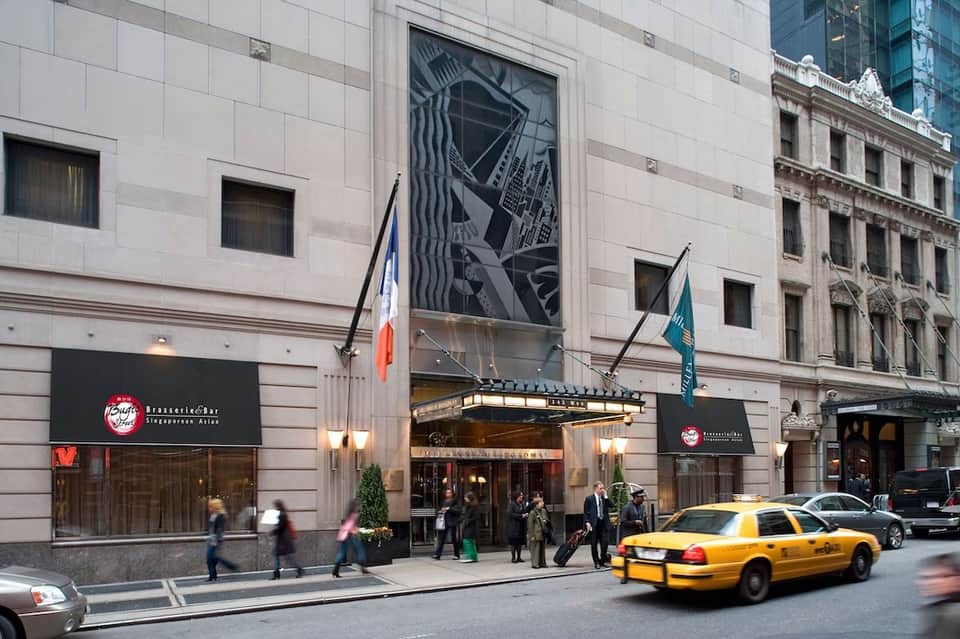 Urban hotel entrance on city street with yellow taxi, flags, and pedestrians