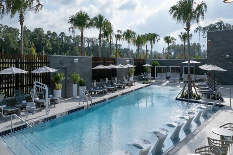Resort pool with umbrellas, lounge chairs, palm trees, spa building, and natural surroundings
