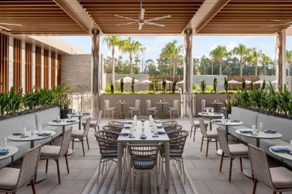 Upscale outdoor dining terrace with pergola, set tables, and palm tree views