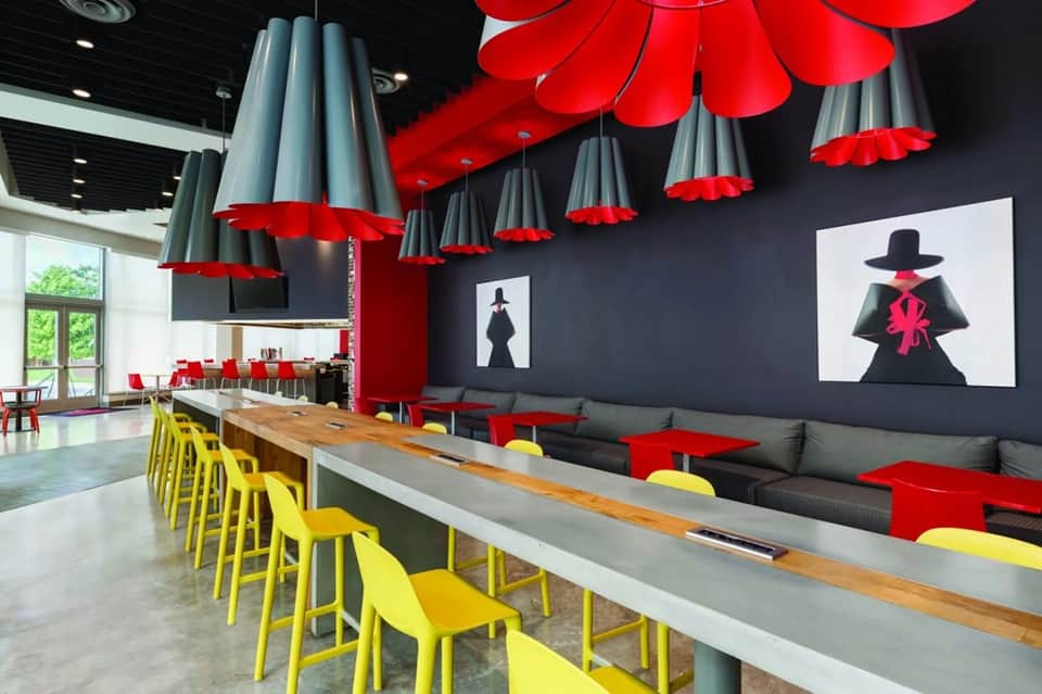 Modern restaurant lounge with red sculptural ceiling pendants, colorful chairs, and artwork