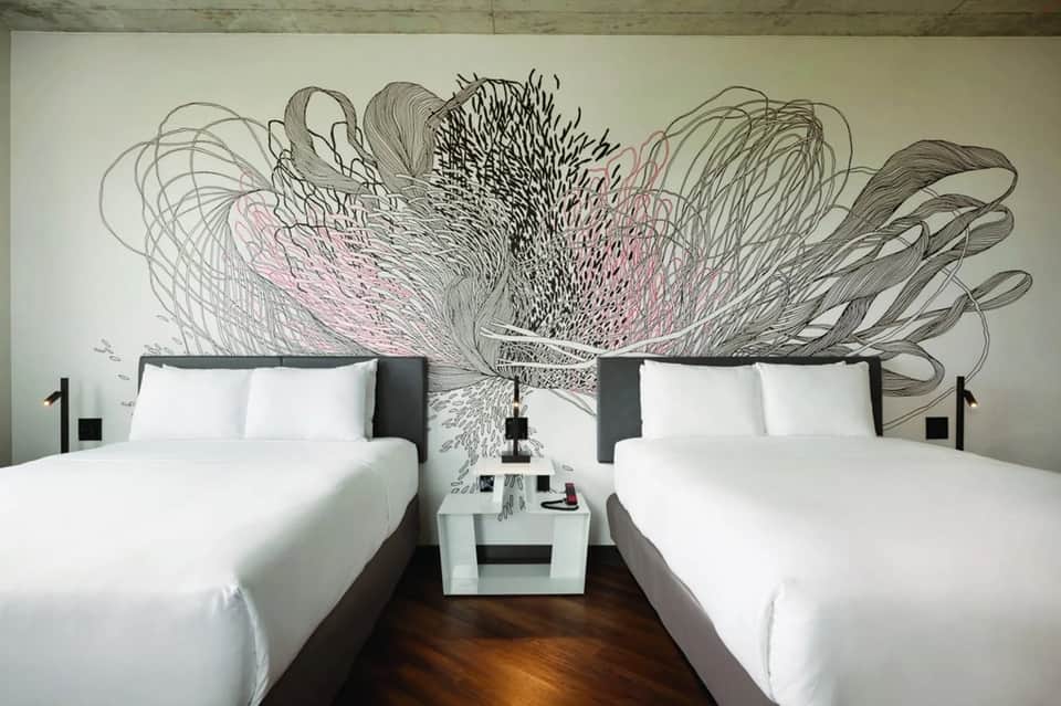 Modern hotel room with two queen beds and artistic black and pink wall mural