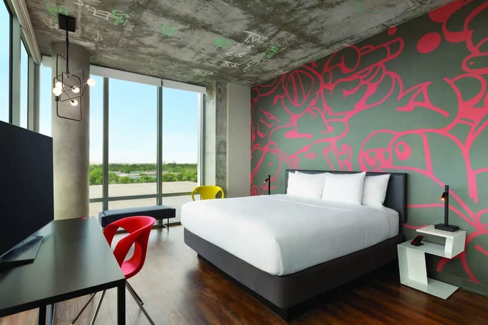 Modern hotel room with bold pink floral wall art, white bed, and panoramic windows