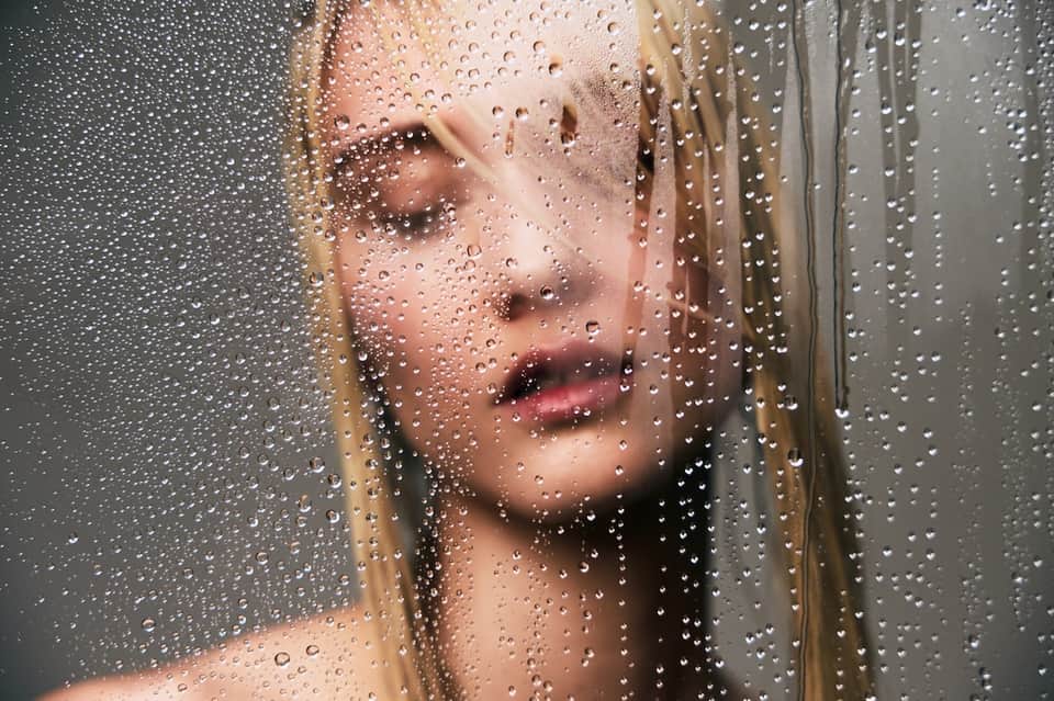 Person showering behind steamed glass shower enclosure with water droplets