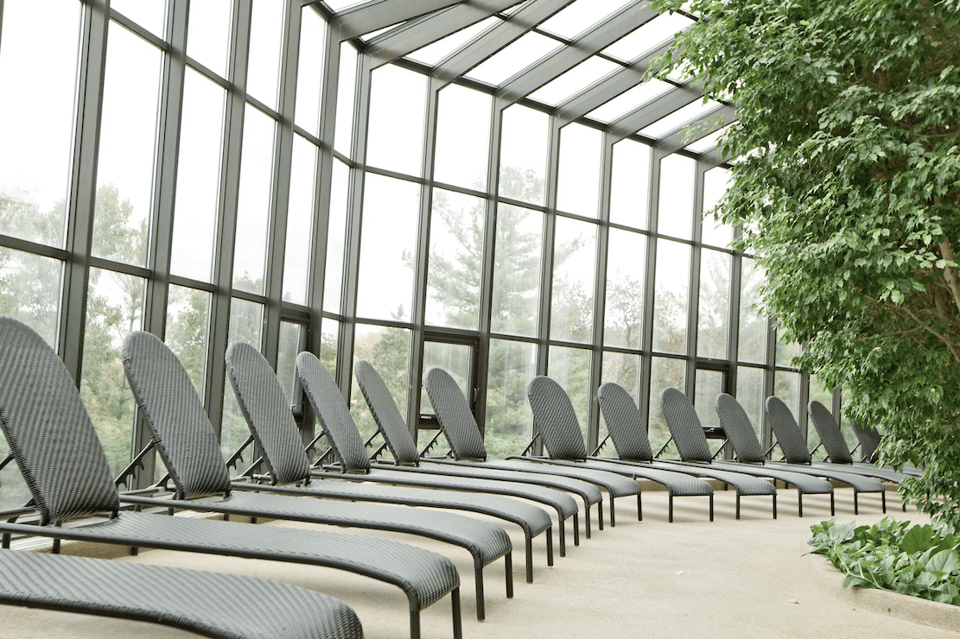 Spa relaxation room with rows of lounge chairs under glass ceiling surrounded by greenery