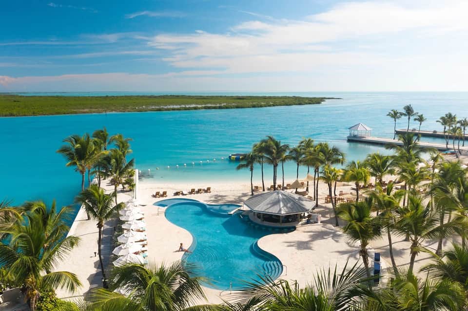 Luxury beachfront resort pool with thatched cabana, pristine beach, turquoise water, and palm trees