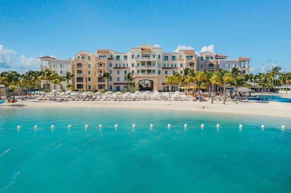 Colorful beachfront resort with multi-story pastel buildings, white sand beach, turquoise water, and palm trees