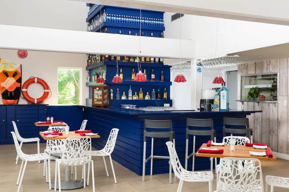 Modern bar and restaurant interior with navy blue bar counter, white chairs, and red pendant lighting fixtures