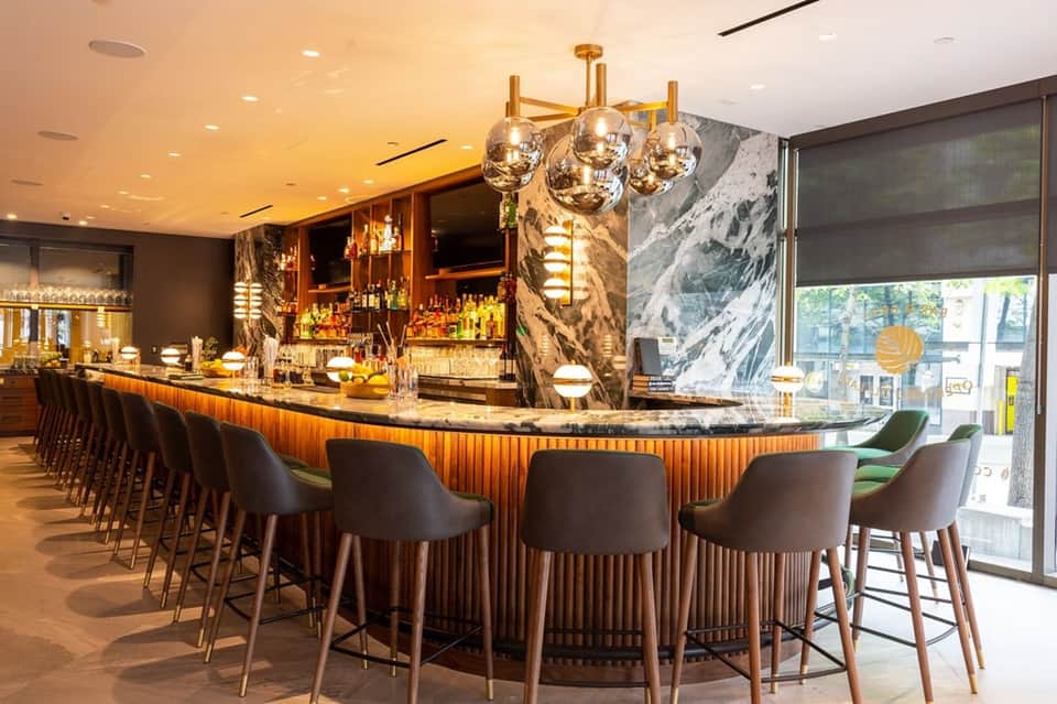 Upscale bar with curved marble counter, bronze pendant lights, and city views through windows