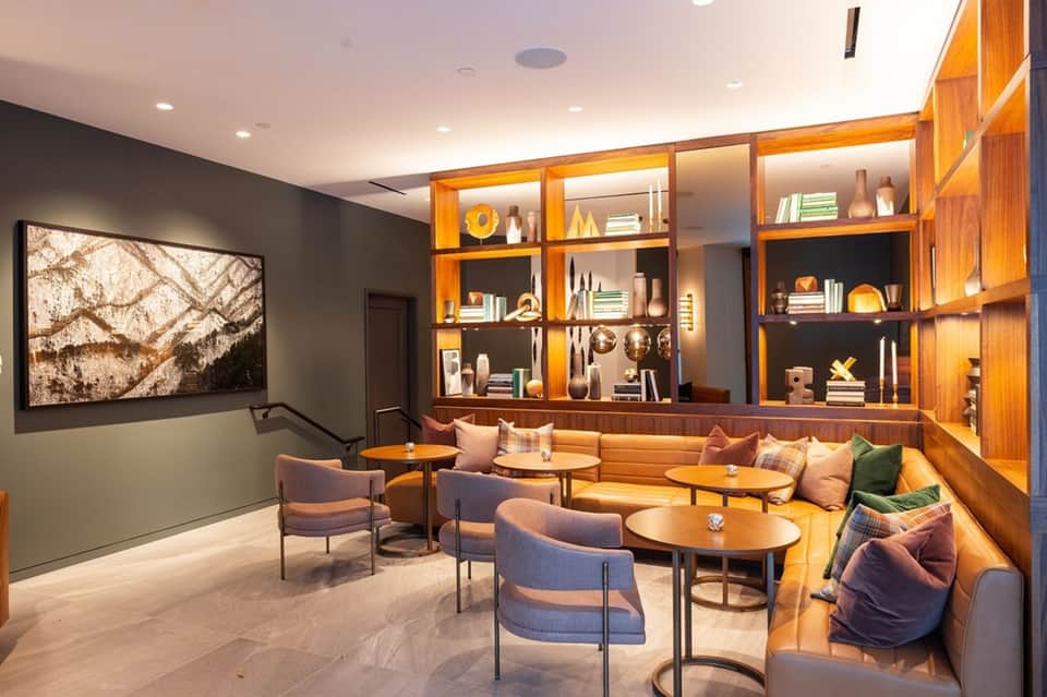 Contemporary lounge with illuminated wooden shelving, gray walls, mid-century furniture, and ambient lighting