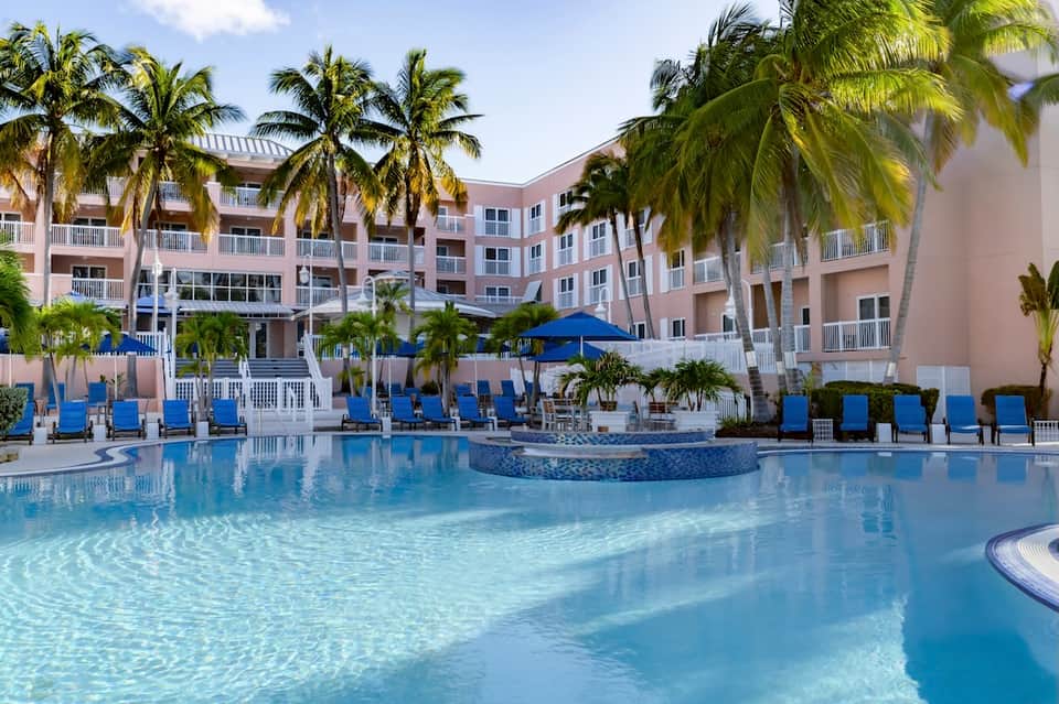 Luxury resort pool with turquoise water, blue umbrellas, loungers, and palm tree landscaping