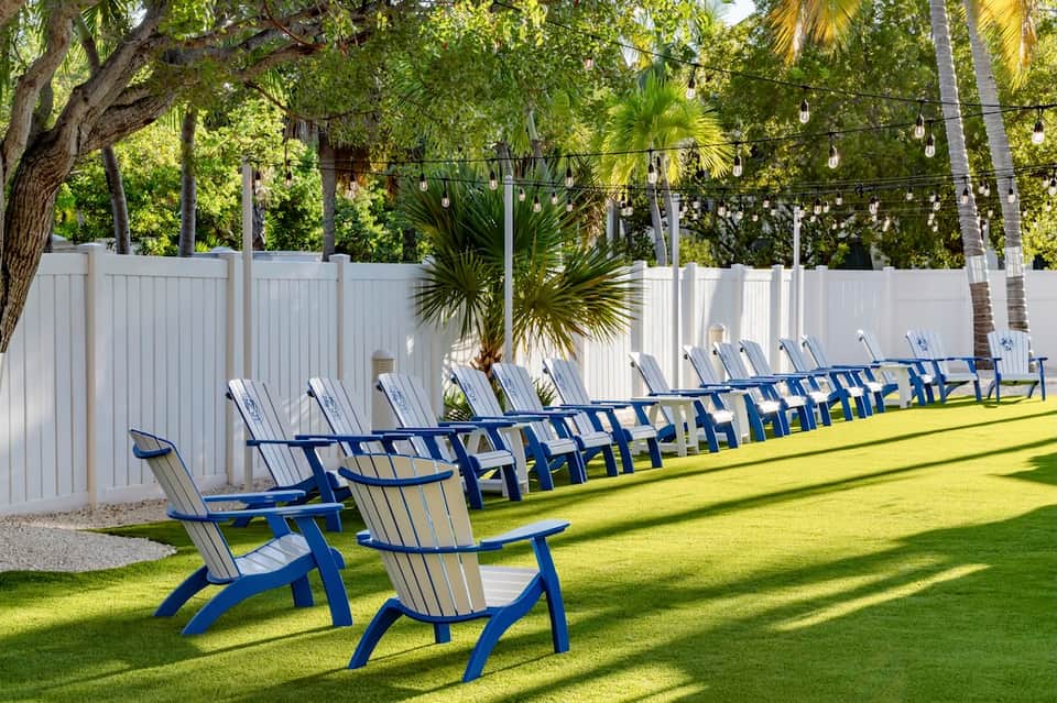Row of blue and white Adirondack chairs on manicured lawn with white privacy fence