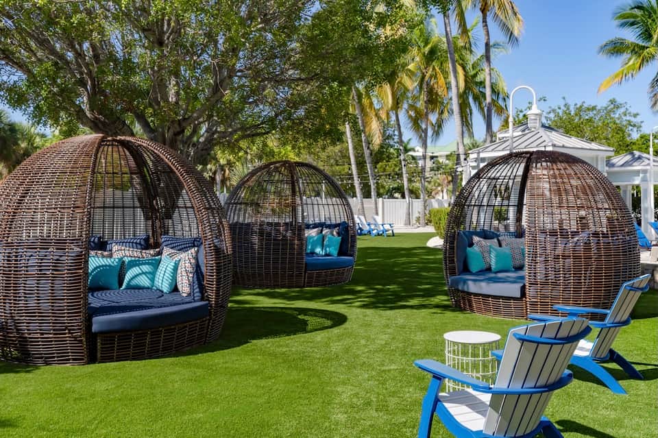 Luxury lawn area with woven egg chair lounges, palm trees, white gazebo, and manicured grass
