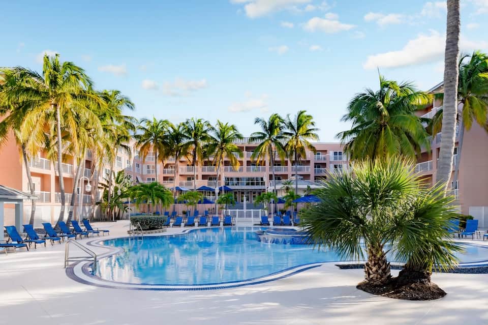Resort pool surrounded by tropical palm trees and residential buildings with blue loungers