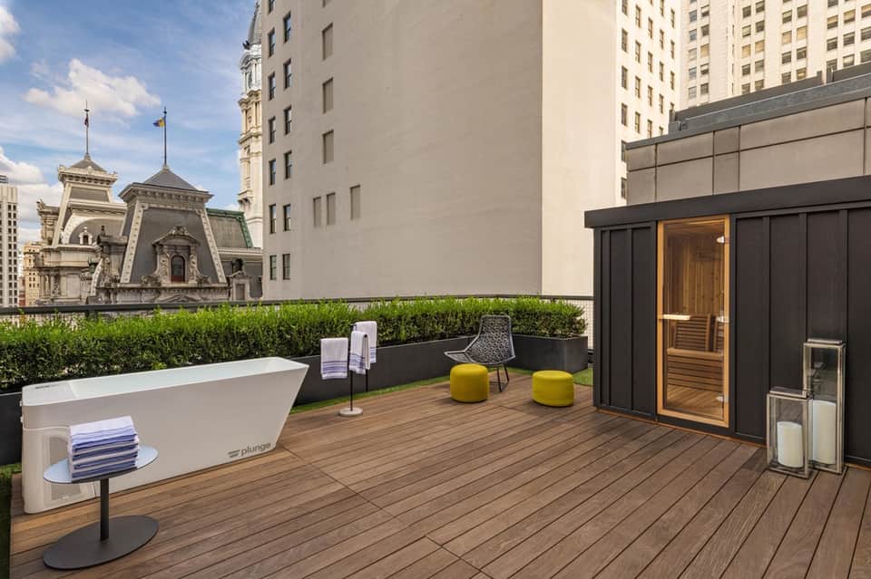 Rooftop terrace with soaking tub, sauna entrance, wood decking, hedge landscaping, and urban views