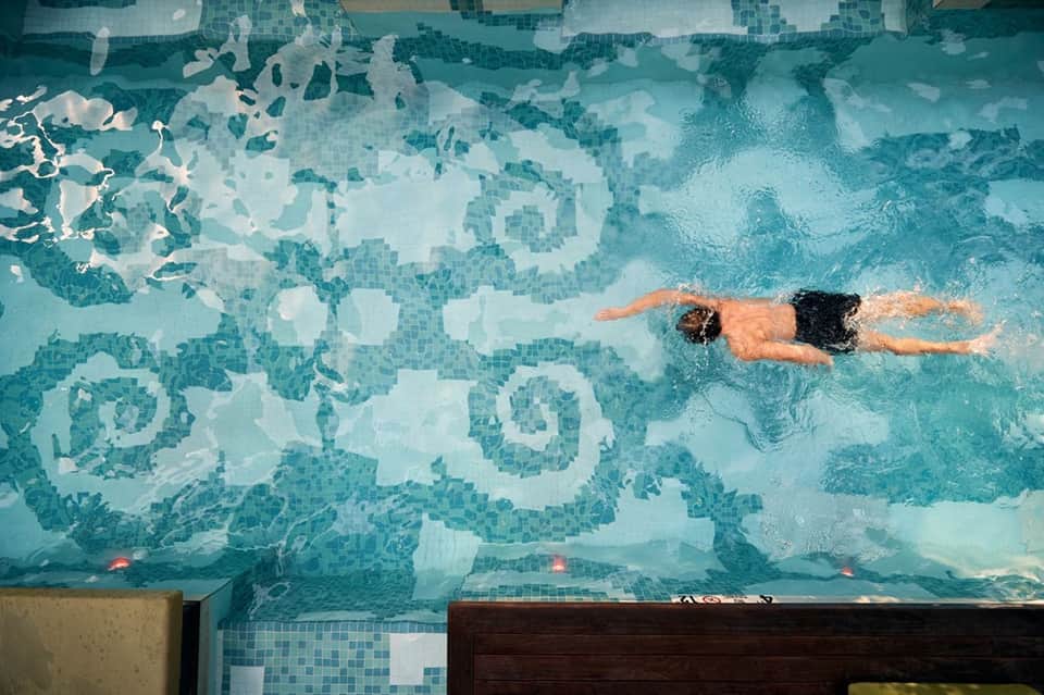 Overhead view of swimmer doing butterfly stroke in indoor pool with decorative tile pattern