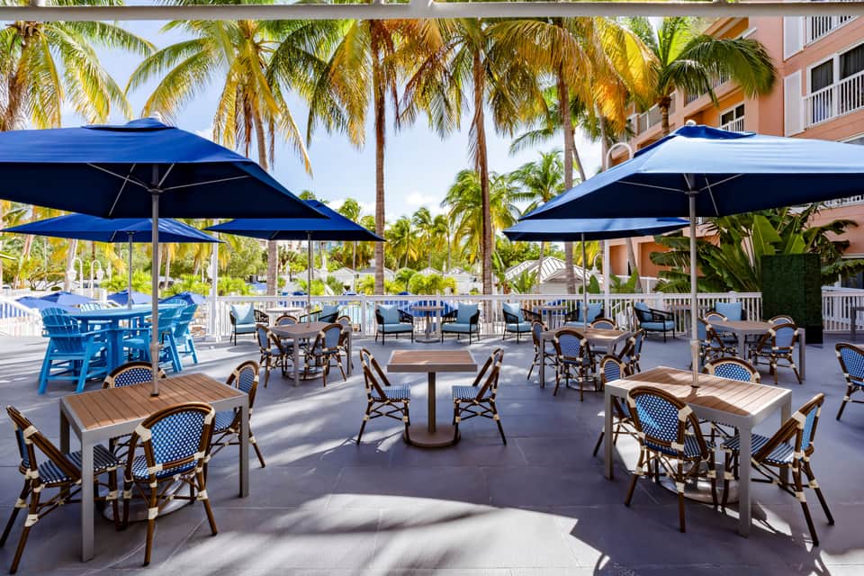 Oceanview terrace with blue umbrellas, dining tables, palm trees, and resort building