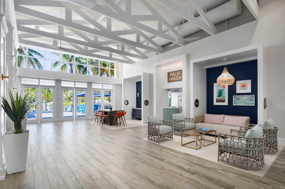 Bright modern lobby with white geometric ceiling, palm trees, blue water views, and contemporary seating area