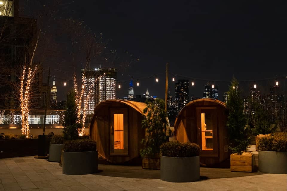Rooftop wooden sauna pods with city skyline at night and illuminated trees