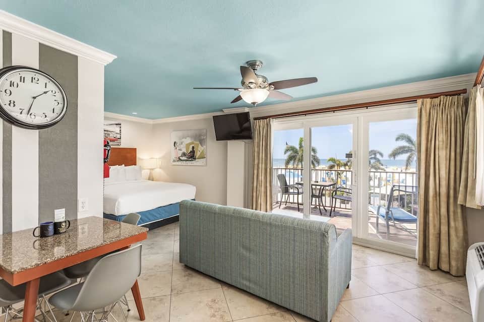 Modern hotel room with turquoise ceiling, white bedding, ocean-view balcony, and contemporary furnishings