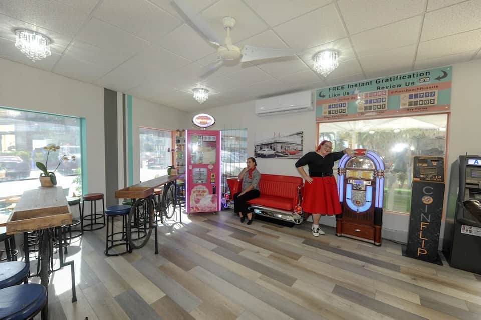 Retro-themed hotel lobby with red sofa, vintage jukebox, vending machines, and bicycle