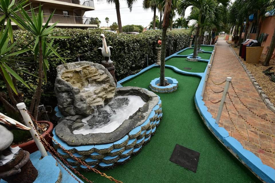 Colorful mini-golf course with tropical landscaping, rock formations, and palm trees