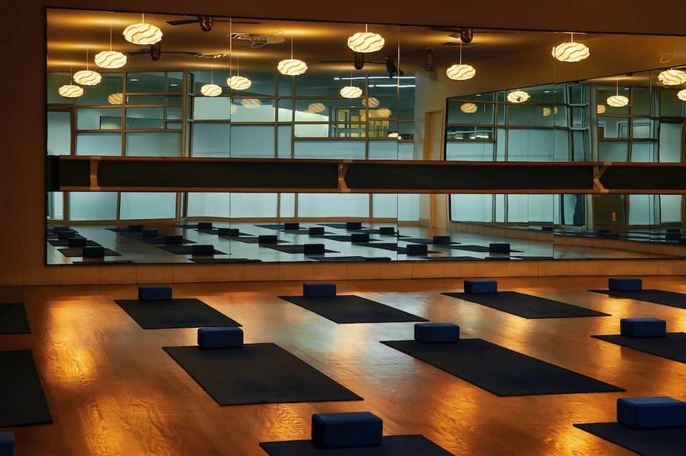 Yoga studio interior with wooden floor, mirrors, pendant lighting, blue bolsters on black yoga mats