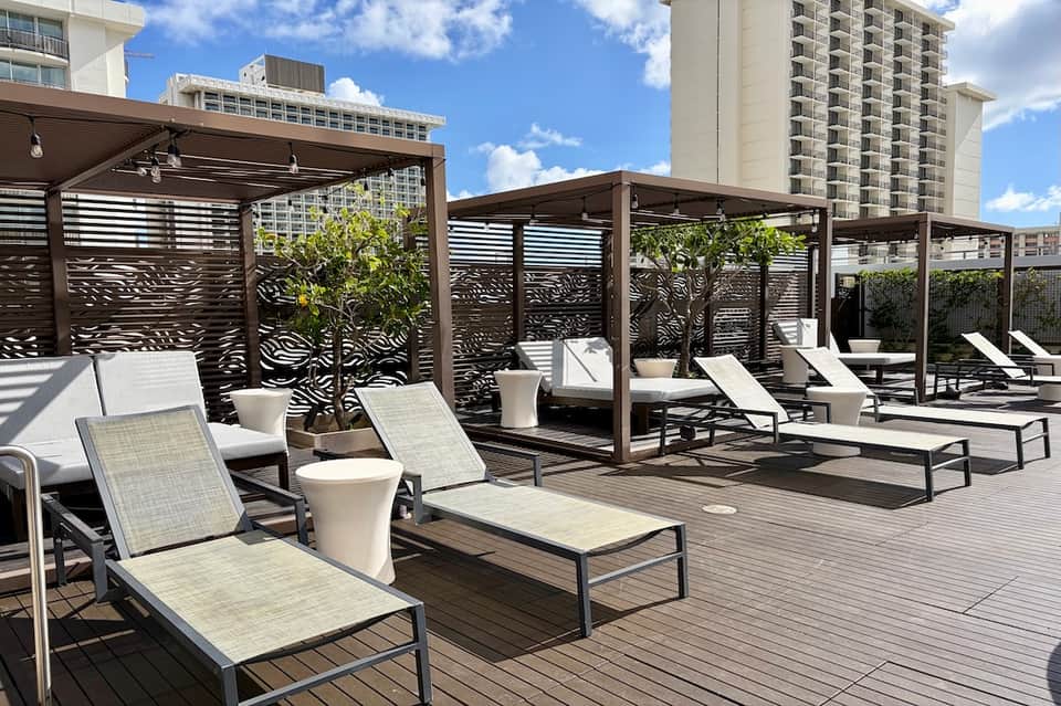 Resort deck with modern lounge chairs, decorative privacy screens, white cylindrical planters, and high-rises