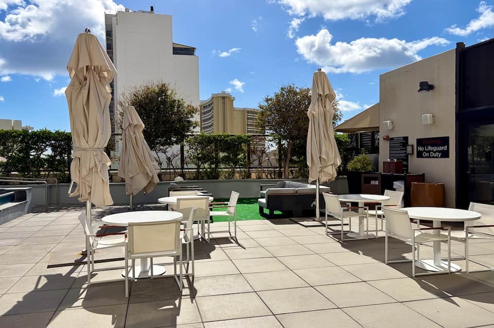 Urban rooftop terrace with lounge seating, umbrellas, artificial turf, and city skyline