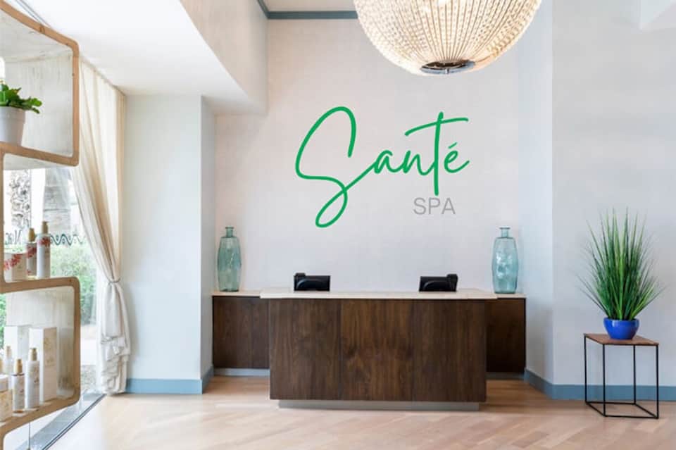 Modern spa reception desk with 'Santé SPA' signage in green, light wood shelving, and minimalist decor