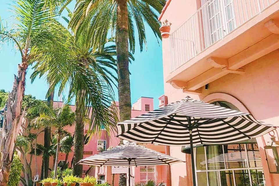 Pink hotel building with striped black and white umbrellas and palm trees in sunny courtyard