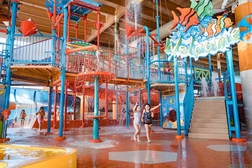 Indoor water park with colorful splash pad, slides, and children playing in shallow water