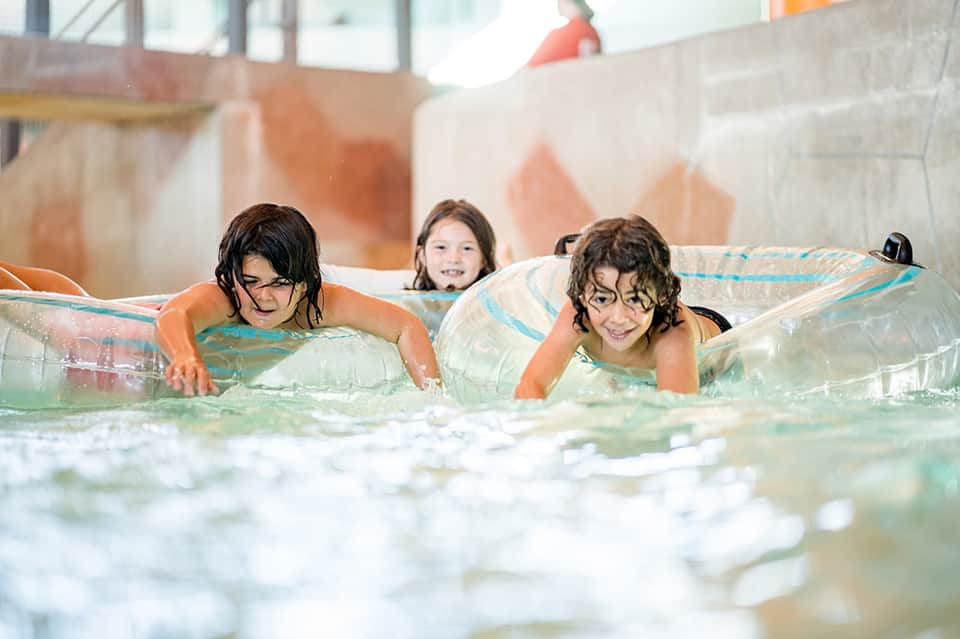 Children enjoying water slides and inflatable toys in indoor resort pool facility