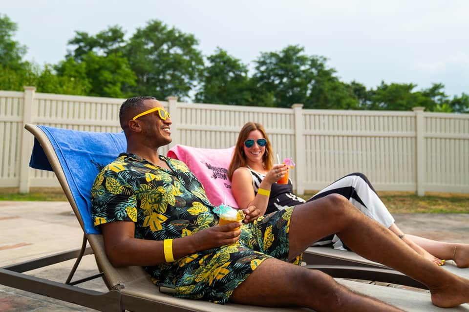 Couple relaxing on lounge chairs on patio with beverage drinks and privacy fencing in background