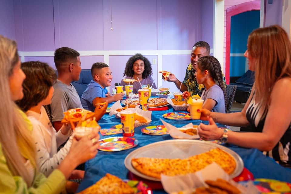 Family dining in colorful kids' game room with pizza, juice, and bright purple walls