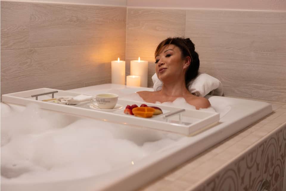 Woman relaxing in spa bath with candles and bath amenities on wooden tray