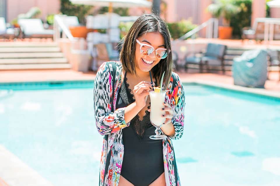 Woman in swimsuit and colorful cardigan holding a cocktail by a resort pool