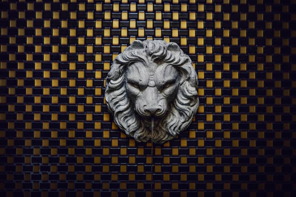 Decorative stone lion head sculpture mounted on geometric gold and navy blue tiled wall panel