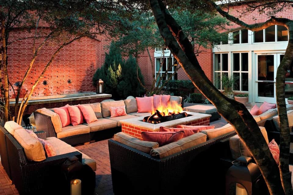 Courtyard fireplace lounge with orange cushioned seating, brick building, fire pit, and candlelight at dusk