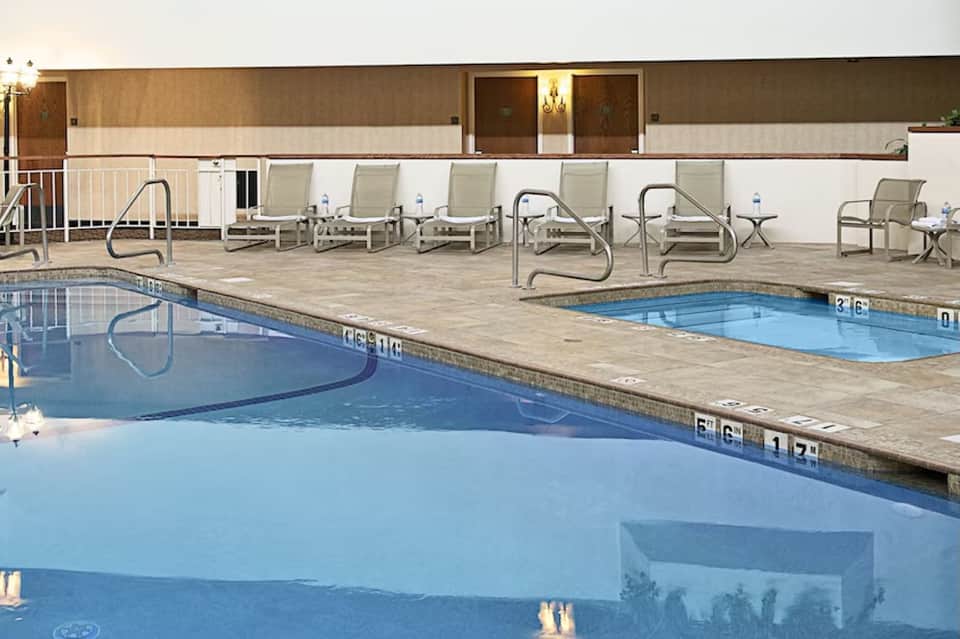 Resort pool deck with two pools, lounge chairs, metal railings, and building with illuminated windows