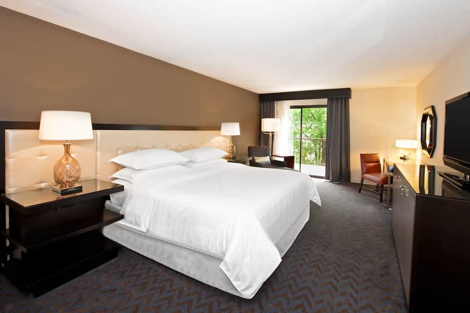 Hotel bedroom with queen bed, neutral décor, bedside lamps, and patio access