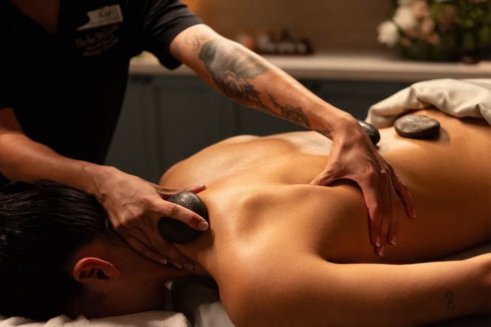 Spa therapist performing stone massage treatment on client's back and shoulders