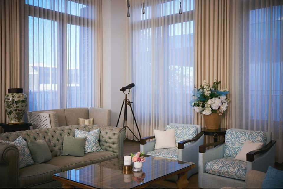 Elegant sitting room with green tufted sofa, armchairs, telescope, white flowers, and floor-to-ceiling sheer curtains