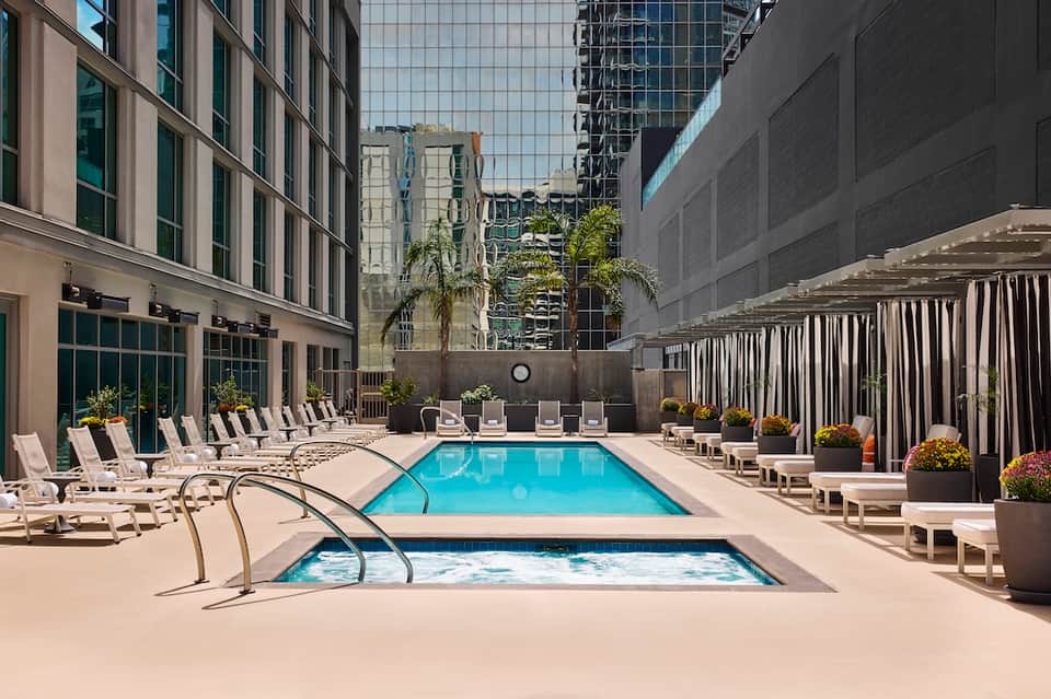 Urban hotel courtyard pool surrounded by white lounge chairs and high-rise buildings
