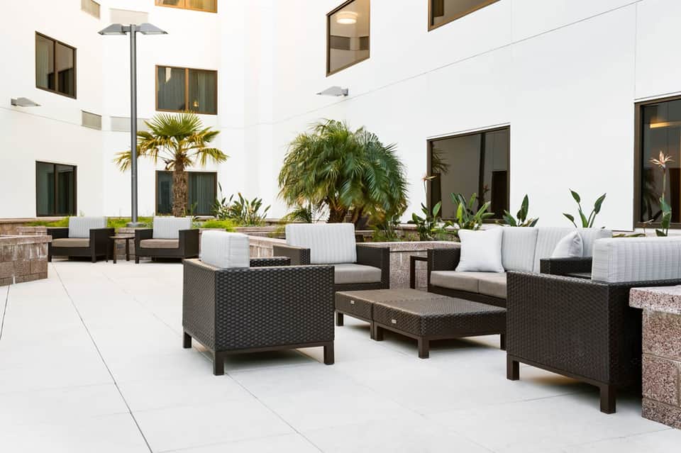 Outdoor courtyard with modern rattan furniture, white cushions, palm trees, and contemporary architecture