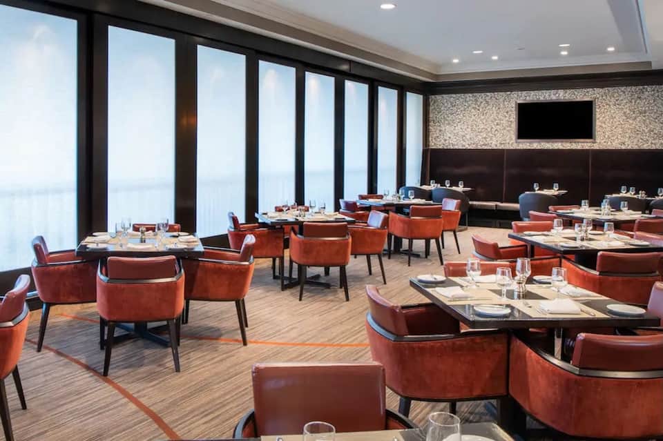 Modern rooftop dining restaurant with floor-to-ceiling windows, ocean views, and red chairs