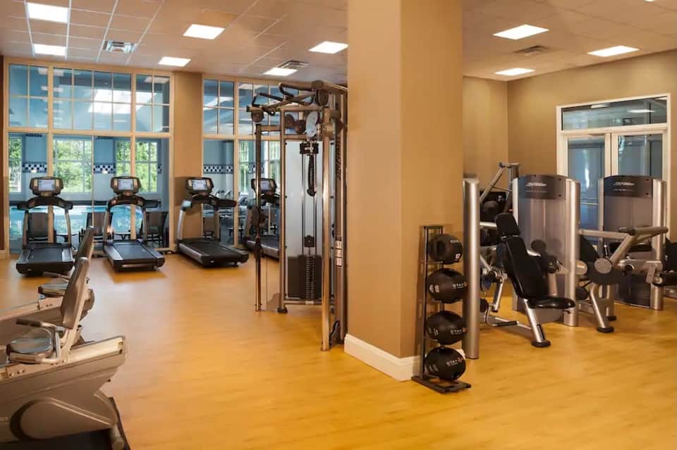 Bright fitness center with exercise equipment, large windows, yellow floors, and mirrored walls