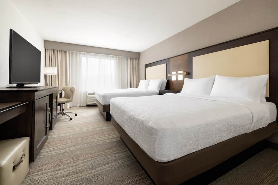 Modern hotel room with two queen beds, desk, TV, and contemporary furnishings
